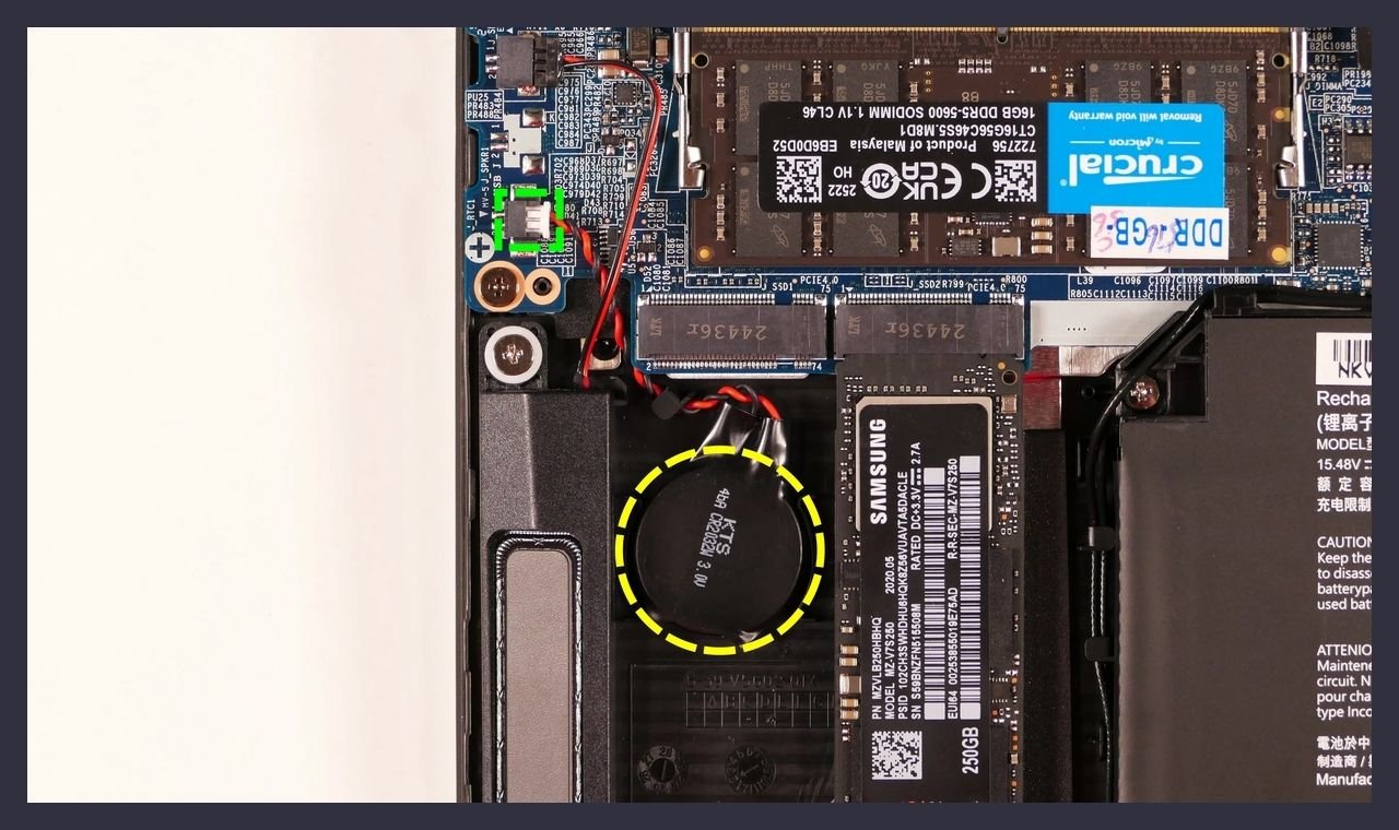 A laptop motherboard with the round CMOS coin cell battery circled in yellow, beside RAM and an M.2 SSD